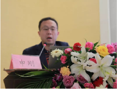 申刚医生在讲台上发言，前方有姓名牌和花束